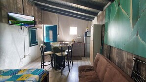 A compact room with a kitchenette, a TV mounted on the wall, a sofa, and a dining area with chairs. - Studio Cadushi, Walking - 10 min from the beach (Noord)