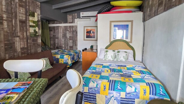 A room with two beds, a table, and a chair. There are two air conditioning units on the wall. - Studio Cadushi, Walking - 10 min from the beach (Noord)