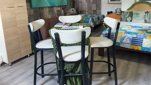 A room with a dining table and chairs, a bed with a colorful bedspread, a green wall with a geometric pattern, and a ceiling with exposed beams. - Studio Cadushi, Walking - 10 min from the beach (Noord)
