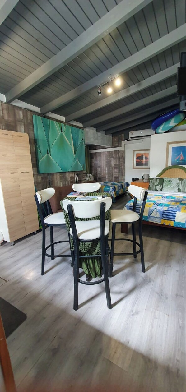 A room with a dining table and chairs, a bed with a colorful bedspread, a green wall with a geometric pattern, and a ceiling with exposed beams. - Studio Cadushi, Walking - 10 min from the beach (Noord)