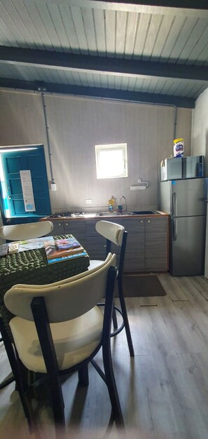 A compact kitchen with a sink, stove, and refrigerator. There is a chair and a table with books. - Studio Cadushi, Walking - 10 min from the beach (Noord)