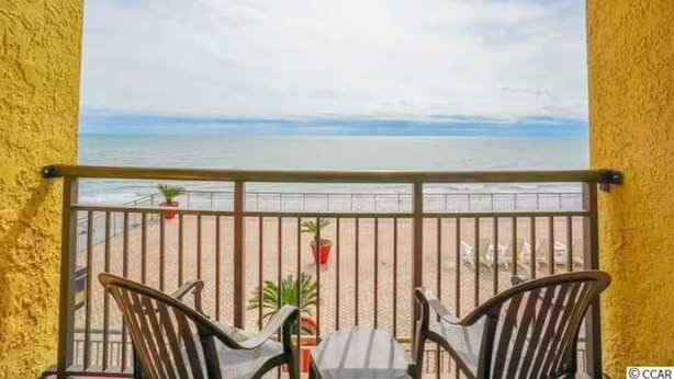 Un balcon avec vue sur la plage, deux chaises et une petite table.