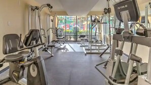 Une salle de sport équipée de machines de cardio, d’appareils de musculation et offrant une vue sur un espace extérieur aux couleurs vives.