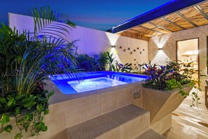 Un área de piscina moderna al aire libre con un jacuzzi, rodeada de plantas exuberantes y un muro de piedra.