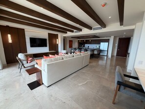 A spacious living area with a large white sofa, a dining area with a kitchen in the background, and a modern ceiling design. - AVAILABLE Luxury Penthouse Suite @ Grand Solmar Pacific Dunes Rancho San Lucas (Cabo San Lucas)