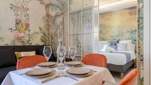 Ein Essbereich mit Tisch für vier Personen, einem Bett im Hintergrund und einem floralen Wanddekor.