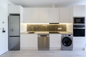 A modern kitchen with white cabinets, a stainless steel dishwasher, a washing machine, and a microwave. - GRAN VIA capitals, VIENA (Madrid)