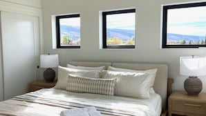 A bedroom with a large bed, two bedside tables, and three windows offering a view of the outdoors. - Sunset Views & Ranch Life ~ Targhee Barndominium (Alta)