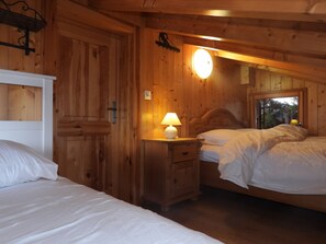 A wooden cabin bedroom with two beds, a nightstand with a lamp, and a window with a view of trees. - Chalet Mirabelle: skiing, hiking or biking from your doorstep (Hérémence)