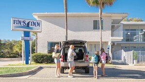 A Fin's Inn sign with a welcome message, a building with a white facade, and a parking area with people and a vehicle. - Bright & Modern Studio • 2 Queen Beds • 3-Min Walk to Beach (Myrtle Beach)