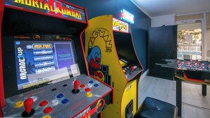 Arcade machines including Mortal Kombat and Pac-Man, a foosball table, and a window with a view of the outside. - Bright & Modern Studio • 2 Queen Beds • 3-Min Walk to Beach (Myrtle Beach)