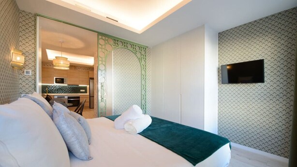 Ein Hotelzimmer mit einem Bett, einer grünen Tagesdecke und einem an der Wand montierten Fernseher.