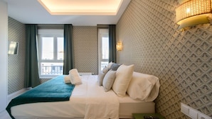 Ein Hotelzimmer mit einem großen Bett, zwei Fenstern, Balkonblick und einer Wandleuchte.