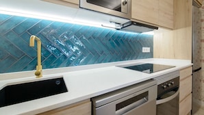 Eine moderne Küche mit weißer Arbeitsplatte, Edelstahlgeräten und einer blau gefliesten Spritzschutzwand.