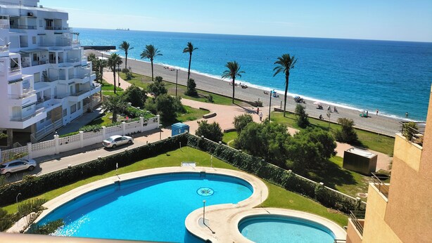 A hotel with a pool, a beach view, and a road with palm trees.