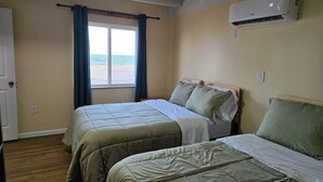 Een kamer met twee bedden, een raam met gordijnen, een airconditioning en uitzicht op het strand.