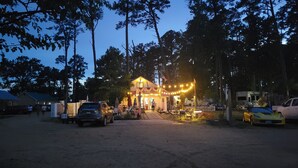 Een rustieke lodge met een onverharde oprit, omringd door hoge bomen en een heldere avondhemel.