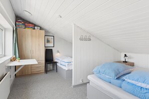 A bedroom with a sloped ceiling, a bed with blue bedding, a desk with a chair, a wardrobe, and a bedside table with a lamp.