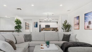 A modern living room with a grey sectional sofa, a coffee table, and a kitchen in the background. - Designer Beach Home, Rooftop Deck, Free Parking, Bike Rentals, King Suites (Newport Beach)