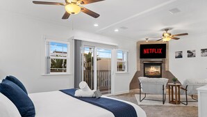A modern hotel room with a large bed, ceiling fans, a fireplace, and a balcony with sliding doors. - Designer Beach Home, Rooftop Deck, Free Parking, Bike Rentals, King Suites (Newport Beach)
