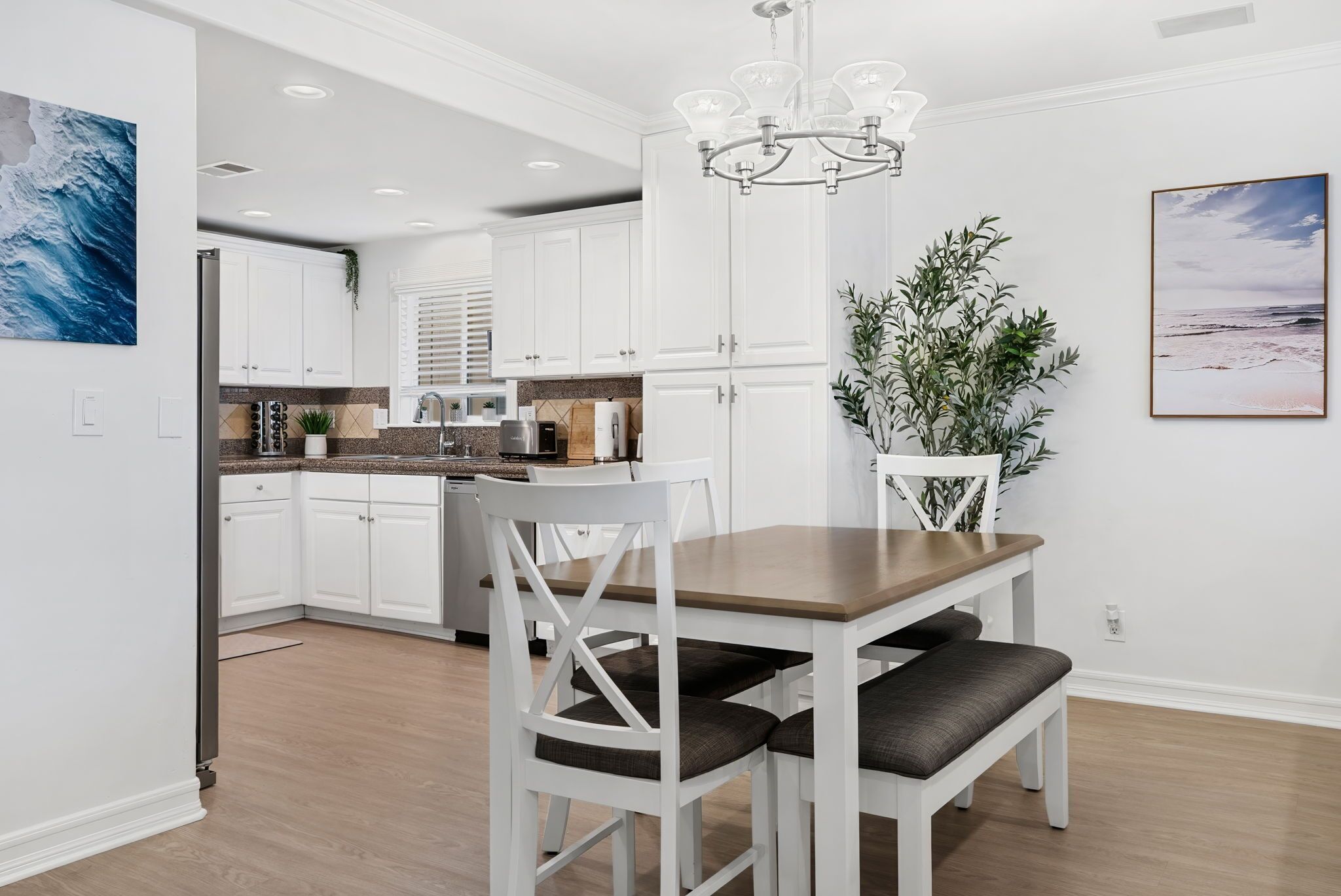 A modern kitchen with white cabinets, a wooden dining table, and a chandelier.
