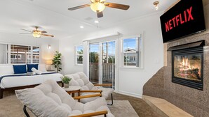 A spacious living room with a fireplace, a ceiling fan, a TV mounted on the wall, and a large window. - Designer Beach Home, Rooftop Deck, Free Parking, Bike Rentals, King Suites (Newport Beach)
