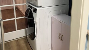 Pesuhuone, jossa on päällekkäin asetetut pesukoneet ja kuivausrummut, puulattia ja vaaleanpunainen kaappi.