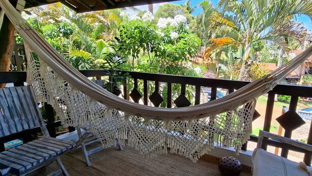 Un hamac sur un balcon, avec vue sur une végétation luxuriante et un bâtiment en arrière-plan.