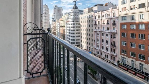Varanda com guarda-corpo de metal, vista para uma rua urbana com edifícios e céu claro.
