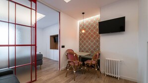 Quarto moderno com área de refeições, TV fixada na parede e papel de parede estampado.
