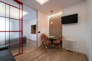 A modern room with a dining area, a TV mounted on the wall, and a patterned wallpaper. - GRAN VIA capitals, LONDREs (Madrid)