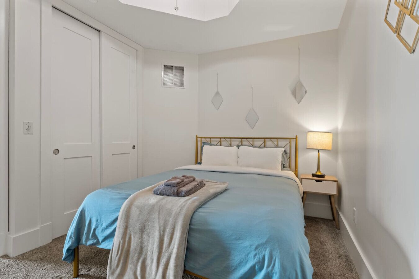 A bedroom with a bed, a bedside table with a lamp, a door, and a wall with geometric decorations.
