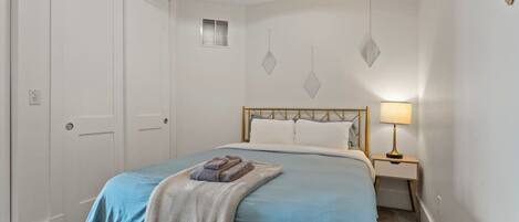 A bedroom with a bed, a bedside table with a lamp, a door, and a wall with geometric decorations.