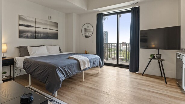 Ein modernes Schlafzimmer mit einem Bett, einem Fernseher und einem Balkon mit Blick auf Gebäude.