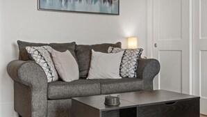 Ein graues Sofa mit gemusterten Kissen, ein dunkles Holz-Couchtisch und ein Stadtbild an der Wand.