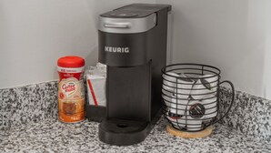 Eine Kaffeemaschine von Keurig, eine Nespresso-Kapsel und eine Metalltasse auf einer Granit Arbeitsplatte.