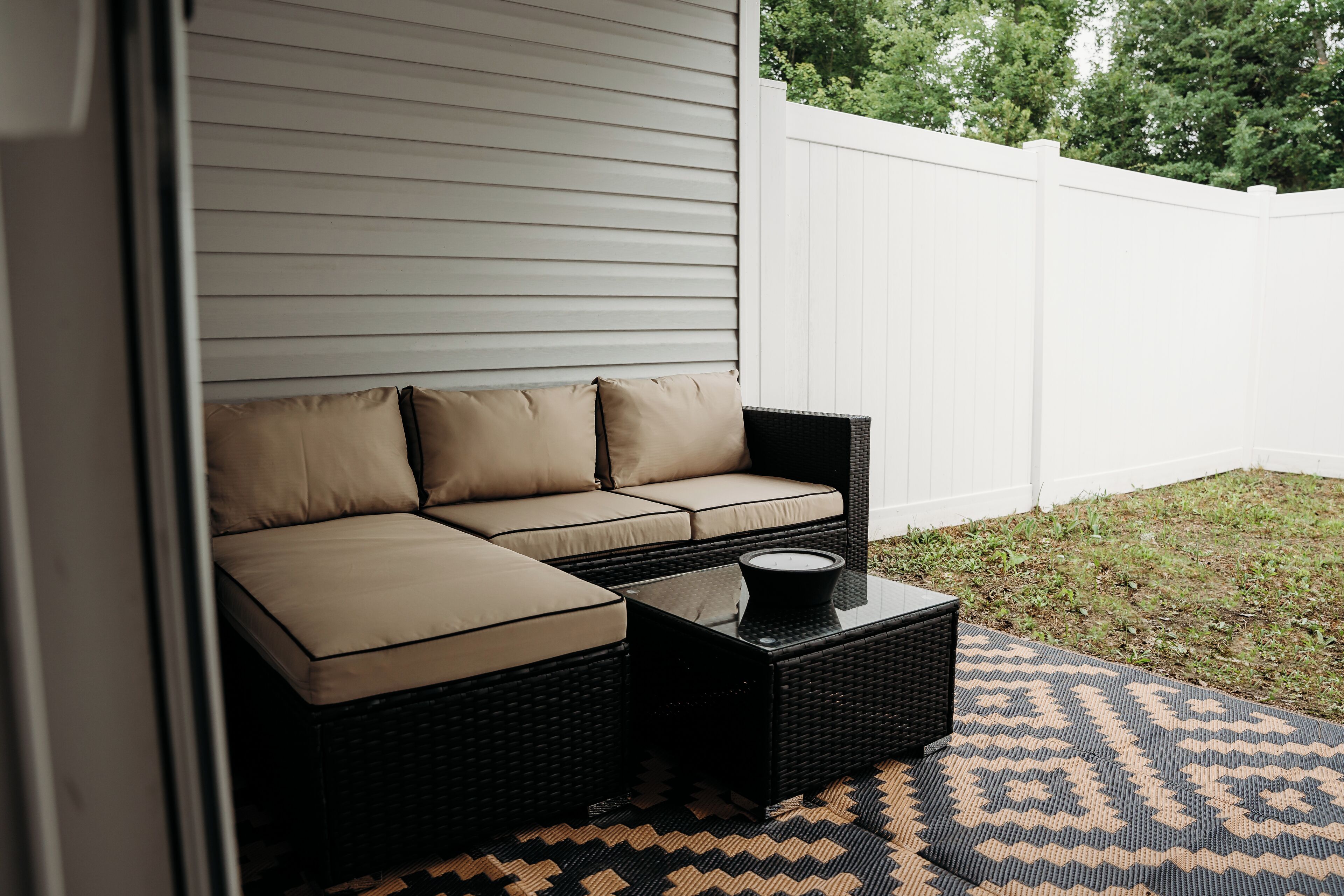A patio area with a black wicker sofa with beige cushions, a small black table, and a patterned rug.