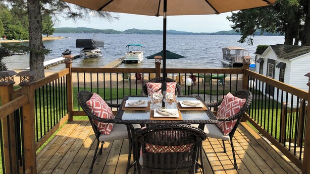 Eine Holzterrasse mit Esstisch, mit Blick auf einen See, auf dem Boote und eine Anlegestelle liegen.