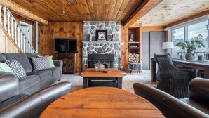 Ein gemütliches Blockhaus-Interieur mit Kamin aus Stein, Ledermöbeln und Holzbalkendecke.