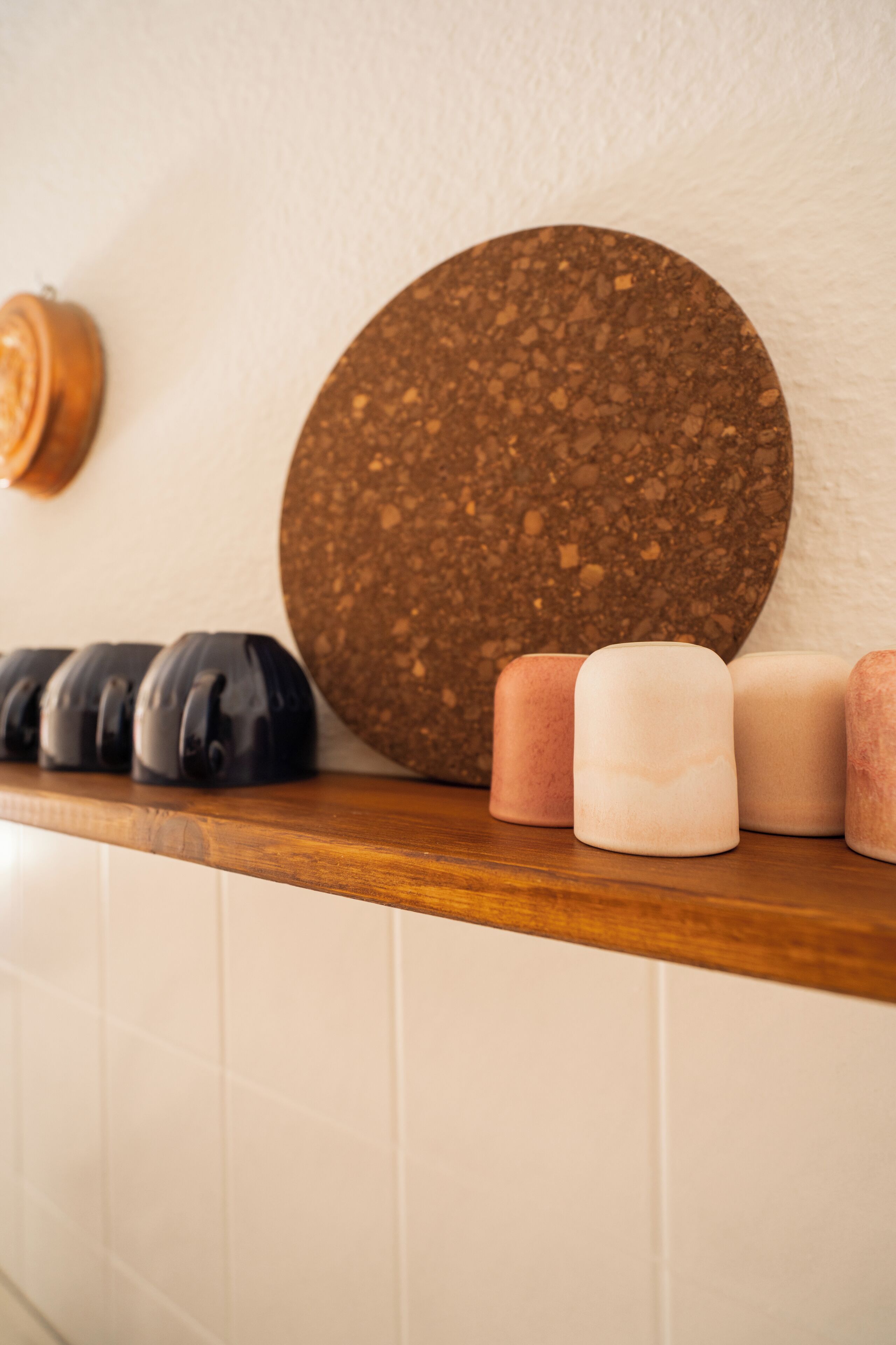 A countertop with a round corkboard, a row of black and pink candles, and a wooden shelf.