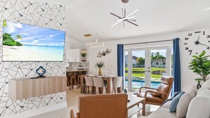 Un soggiorno moderno con televisore, zona pranzo e vista su una piscina.