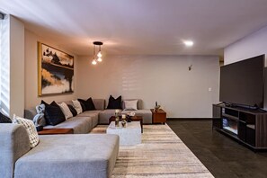 A modern living room with a sectional sofa, a coffee table, a TV, and a painting on the wall. - Del Valle Getaway: Workspace and  Secure Parking (Mexico City)