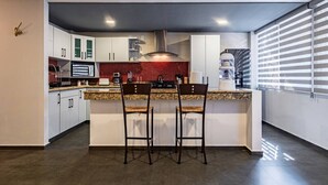 Eine moderne Küche mit Granit-Arbeitsplatten, zwei Barhocker, weißen Schränken und einer roten Spritzschutzleiste.