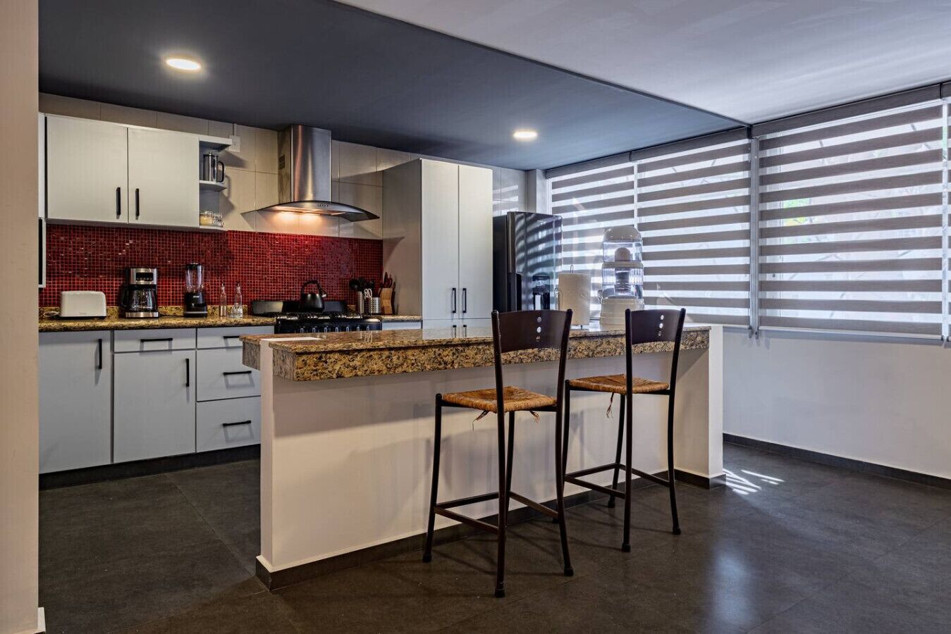 A modern kitchen with white cabinets, a red backsplash, and a large island with bar stools.