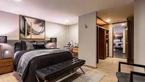 Ein modernes Schlafzimmer mit einem großen Bett, Nachttischen, einer Bank, einem Schreibtisch und einem begehbaren Kleiderschrank.