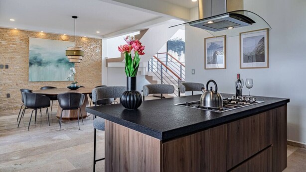 Une cuisine moderne dotée d’un grand îlot central, d’un coin repas avec des chaises, d’un escalier et d’œuvres d’art accrochées aux murs.