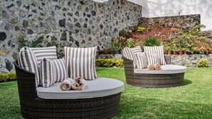 Deux canapés d’extérieur en osier, dotés de coussins à rayures, sont placés sur une pelouse bien entretenue, avec un mur en pierre et des plantes en pot en arrière-plan.