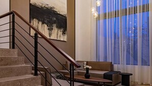 Un intérieur moderne avec un escalier, une grande peinture abstraite, un canapé et un lustre.