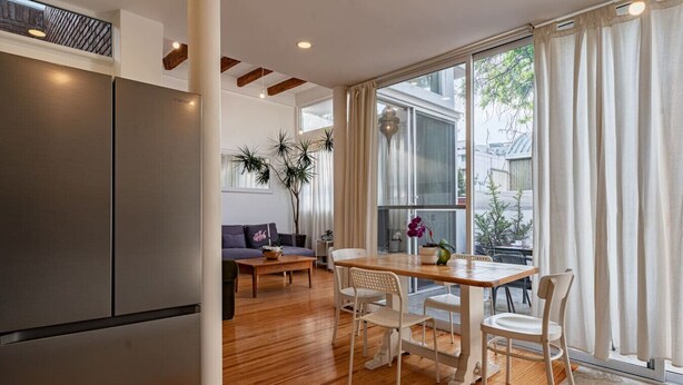 A modern kitchen with a large refrigerator, wooden flooring, and a dining area with a table and chairs.