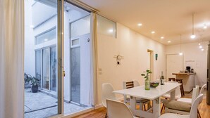 A dining area with a white table and chairs, a small kitchen area, and a sliding glass door leading to an outdoor space with a bicycle.